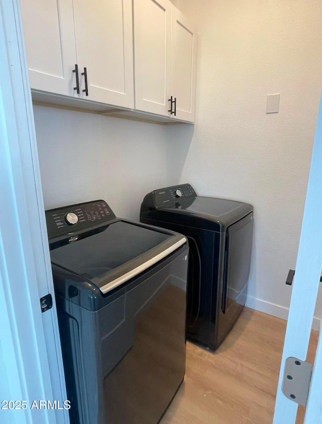 laundry area featuring light wood-type flooring, cabinet space, washer and clothes dryer, and baseboards