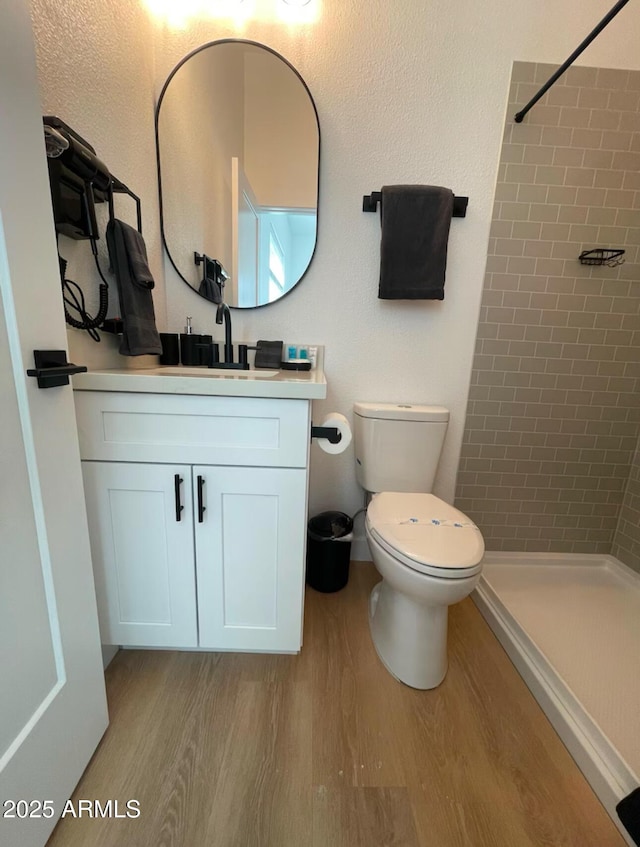 bathroom with toilet, vanity, wood finished floors, and tiled shower