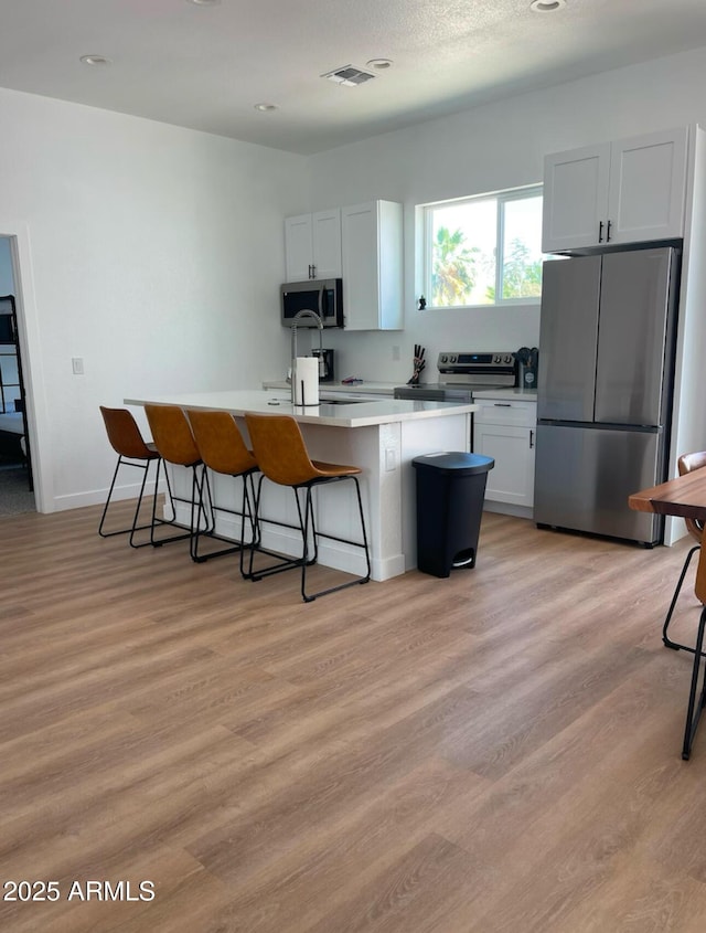 kitchen featuring appliances with stainless steel finishes, light wood-type flooring, a kitchen island with sink, and a kitchen breakfast bar