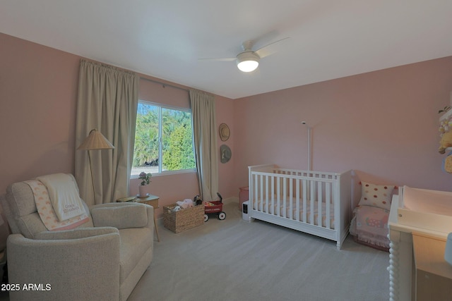 bedroom with a crib, ceiling fan, and light colored carpet