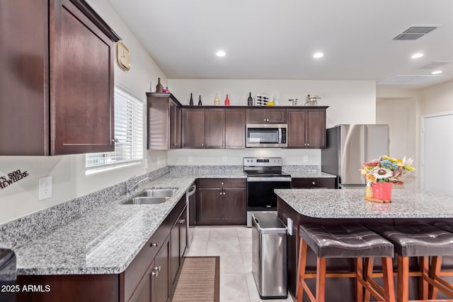 kitchen with a breakfast bar, sink, a center island, stainless steel appliances, and light stone countertops