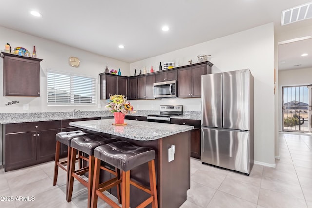 kitchen with a breakfast bar area, dark brown cabinets, stainless steel appliances, a center island, and plenty of natural light