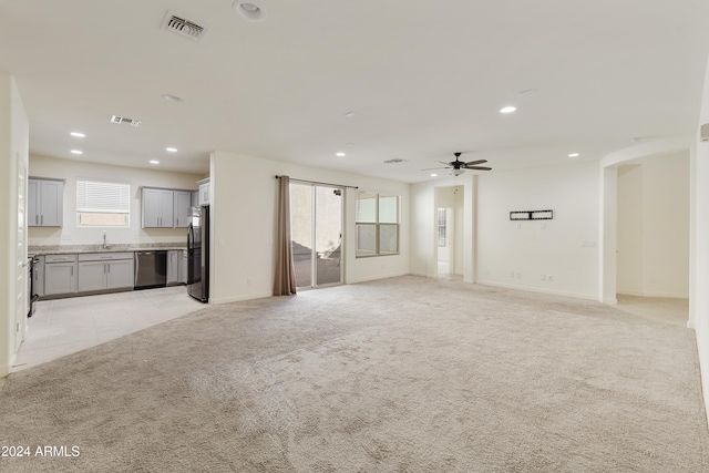 unfurnished living room with sink, light colored carpet, and a healthy amount of sunlight