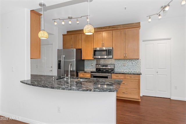 kitchen featuring stainless steel appliances, a sink, decorative backsplash, dark stone countertops, and pendant lighting