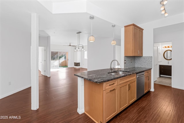 kitchen featuring dark stone counters, dishwasher, open floor plan, decorative light fixtures, and a sink