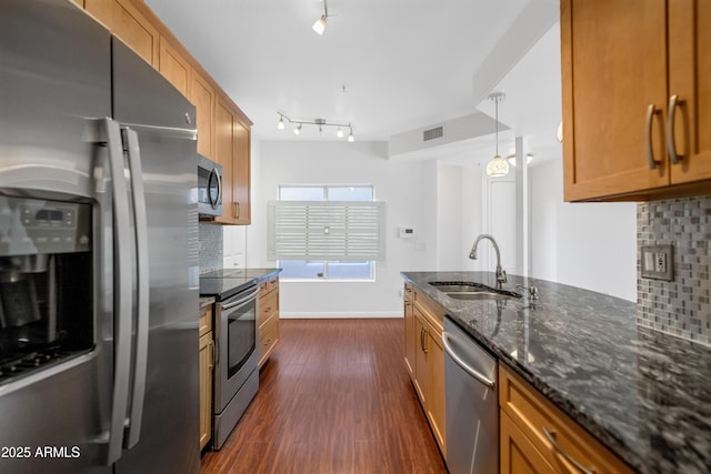 kitchen with dark wood finished floors, hanging light fixtures, appliances with stainless steel finishes, a sink, and dark stone countertops