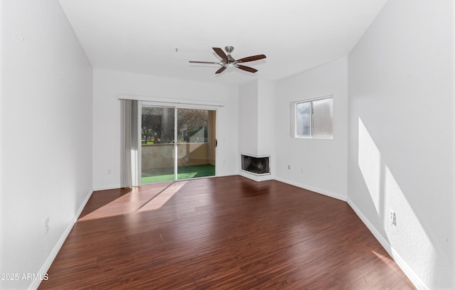 unfurnished living room featuring ceiling fan, dark wood-style flooring, a multi sided fireplace, and baseboards