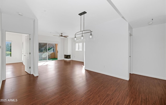 unfurnished living room with dark wood-style flooring, a ceiling fan, and baseboards