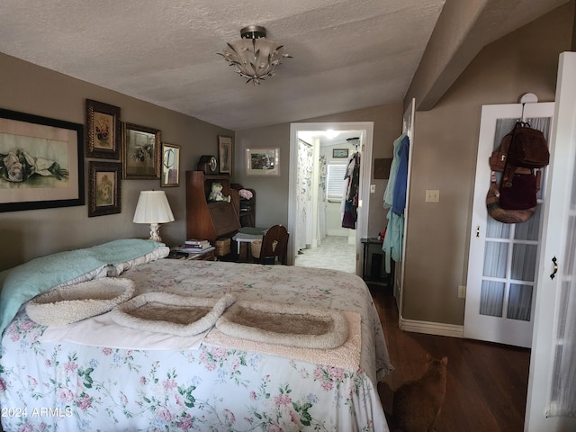 bedroom featuring a walk in closet, a textured ceiling, dark hardwood / wood-style flooring, and lofted ceiling