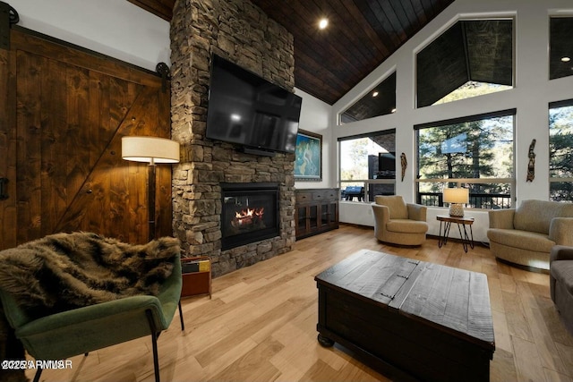 living room with high vaulted ceiling, a fireplace, wood ceiling, light hardwood / wood-style floors, and a barn door