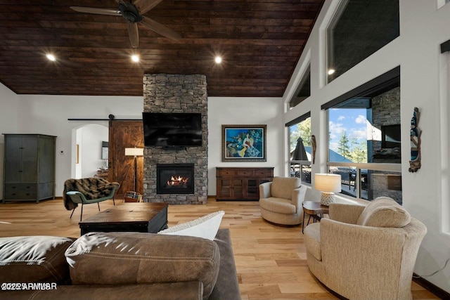 living room with high vaulted ceiling, light hardwood / wood-style floors, a stone fireplace, wooden ceiling, and a barn door