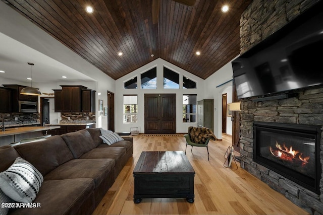 living room featuring wood ceiling, a stone fireplace, high vaulted ceiling, and light wood-type flooring