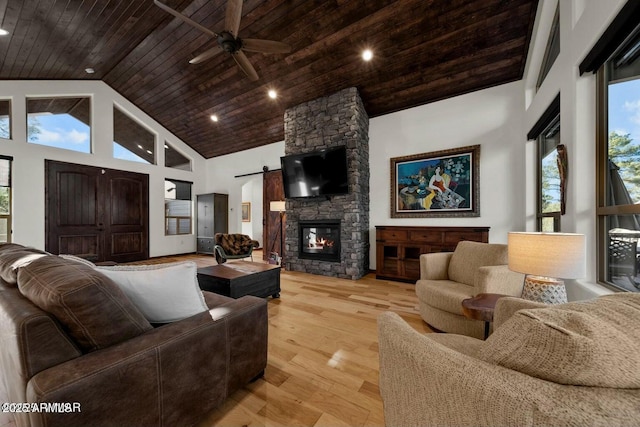 living room with a stone fireplace, wood ceiling, high vaulted ceiling, light wood-type flooring, and a barn door