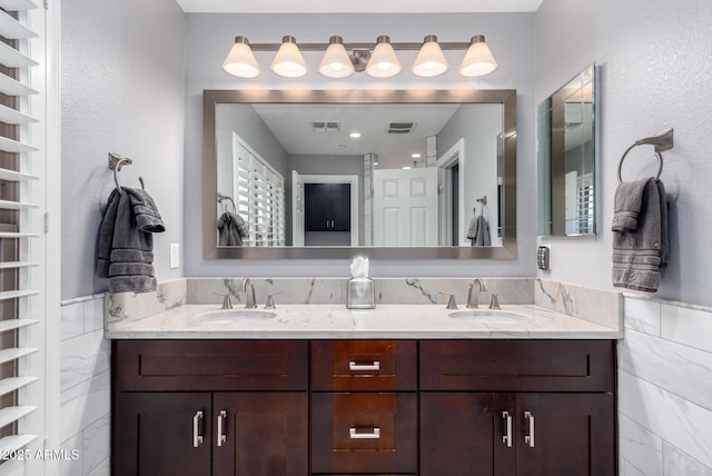 bathroom with tile walls, double vanity, visible vents, and a sink