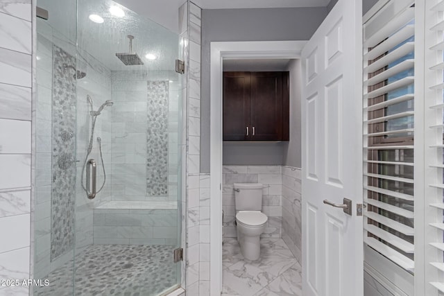 full bath featuring a shower stall, wainscoting, tile walls, toilet, and marble finish floor