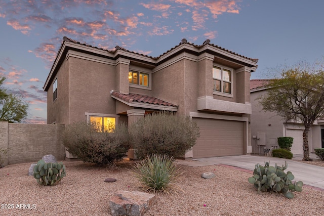 mediterranean / spanish-style house with stucco siding, driveway, a tile roof, fence, and a garage