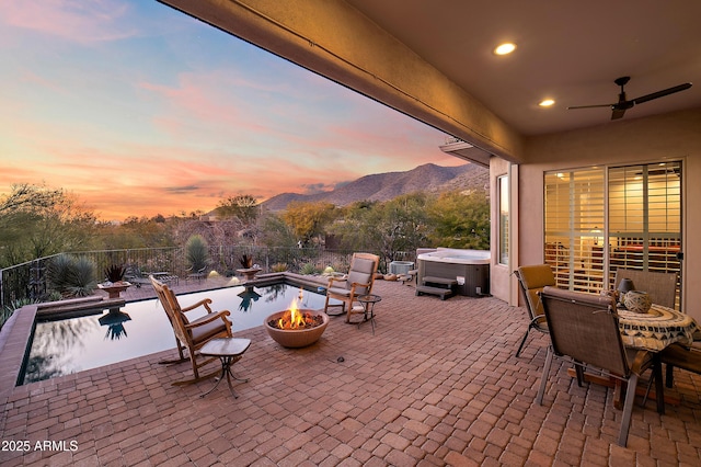 patio terrace at dusk with ceiling fan, a hot tub, and a mountain view