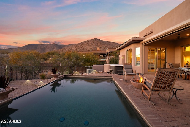 pool at dusk with a mountain view, a patio area, a hot tub, and an outdoor fire pit