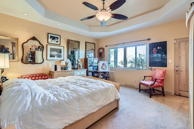 carpeted bedroom with a raised ceiling and ceiling fan