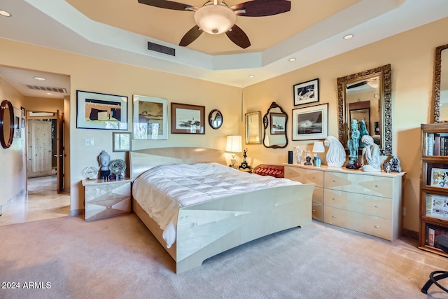 bedroom with ceiling fan, light carpet, and a tray ceiling