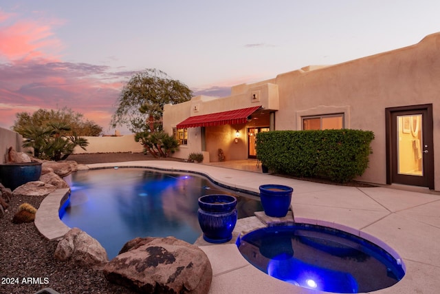 pool at dusk featuring a patio area and an in ground hot tub