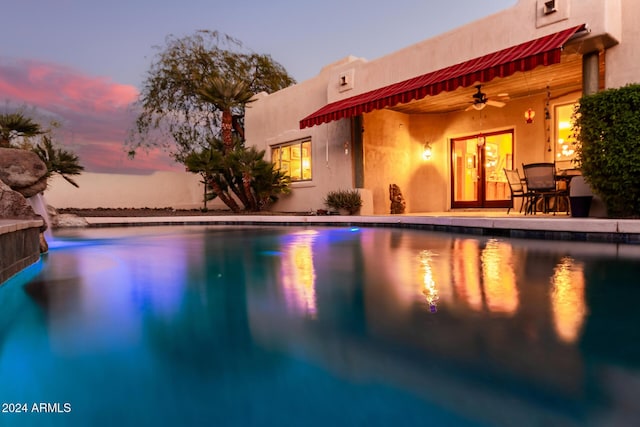 pool at dusk featuring ceiling fan and a patio area