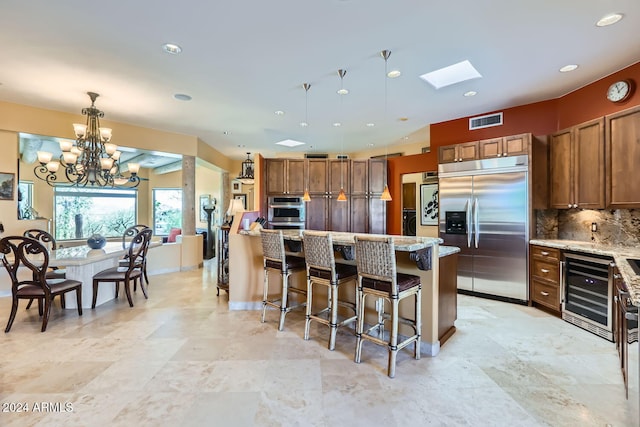 kitchen with light stone counters, pendant lighting, stainless steel appliances, and a notable chandelier