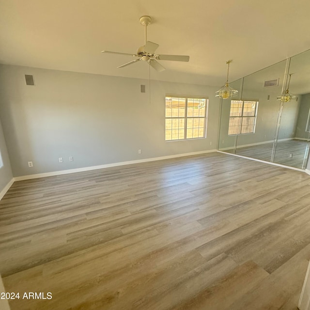 empty room featuring ceiling fan with notable chandelier, vaulted ceiling, and light hardwood / wood-style flooring