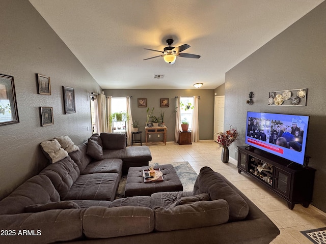 living area featuring light tile patterned floors, visible vents, a ceiling fan, a textured wall, and lofted ceiling