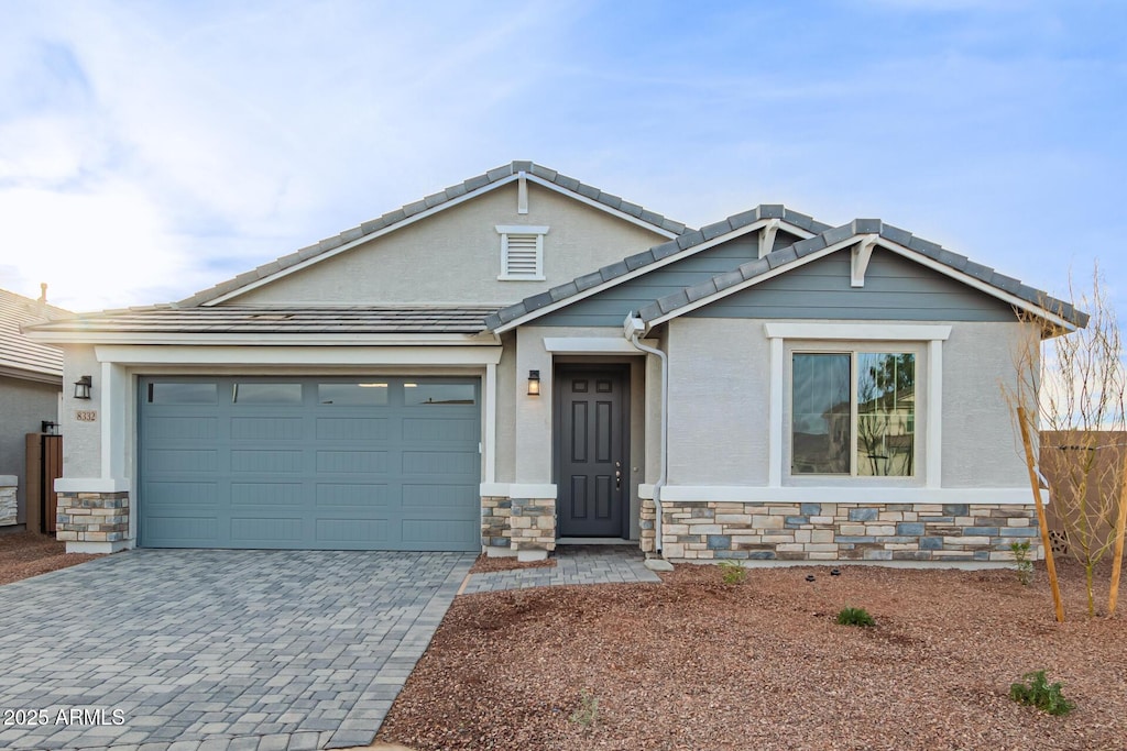 8332 N 54th Ln, Glendale, AZ 85302 - craftsman-style house featuring a tiled roof, stucco siding, decorative driveway, stone siding, and a garage