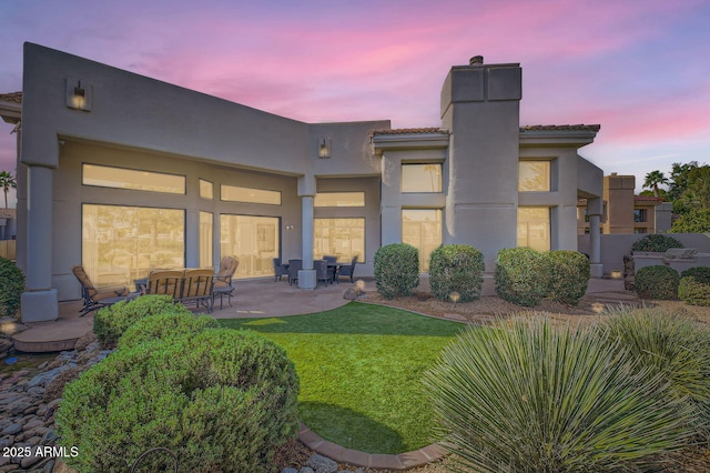 back house at dusk with a yard and a patio