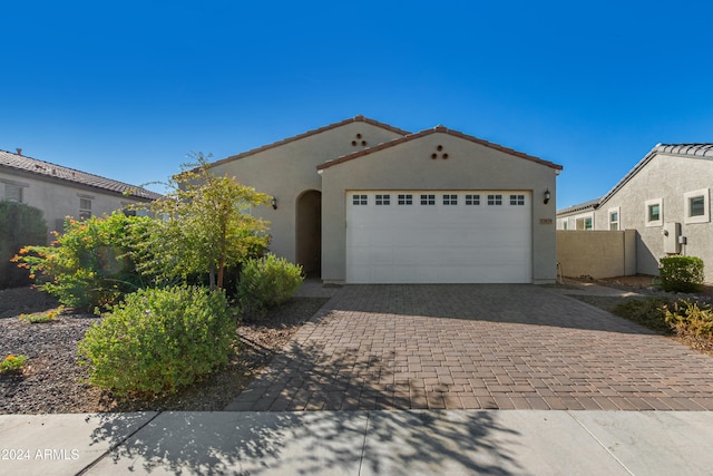 mediterranean / spanish home featuring a tiled roof, stucco siding, an attached garage, and decorative driveway