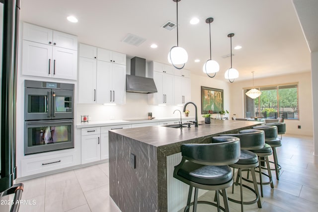 16772 W Cypress St, Goodyear, AZ 85395 - kitchen featuring wall chimney exhaust hood, double oven, a sink, a center island with sink, and a breakfast bar area