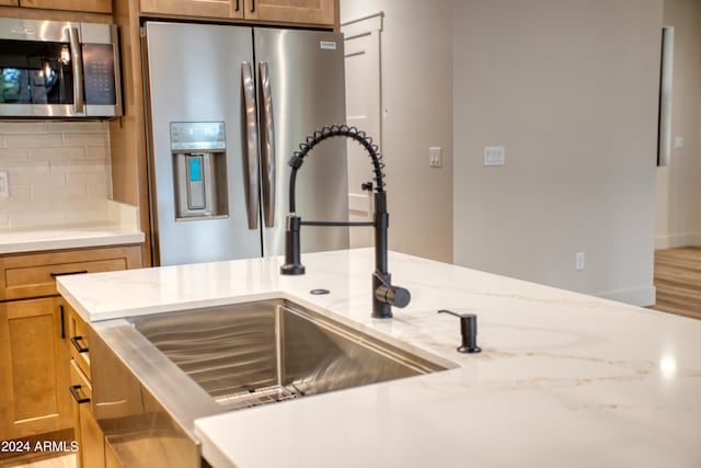 room details featuring light stone counters, a sink, appliances with stainless steel finishes, decorative backsplash, and brown cabinetry