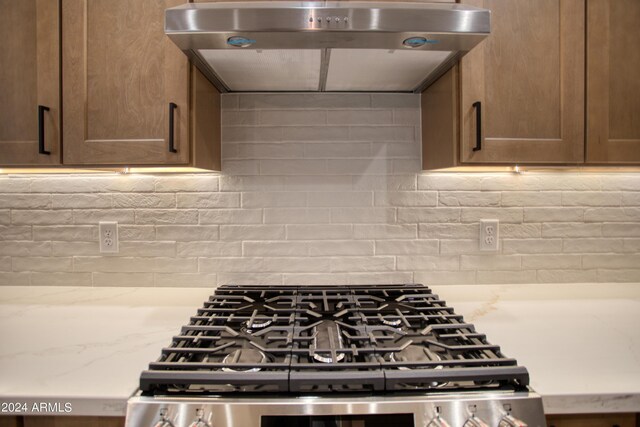 kitchen featuring range hood, stainless steel range with gas cooktop, light stone counters, and tasteful backsplash