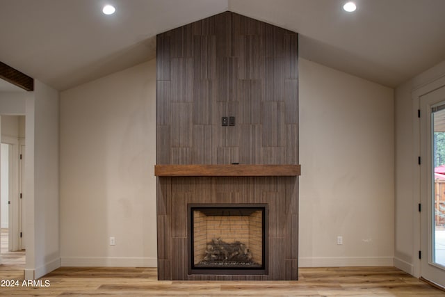 unfurnished living room featuring a large fireplace, vaulted ceiling, and wood finished floors