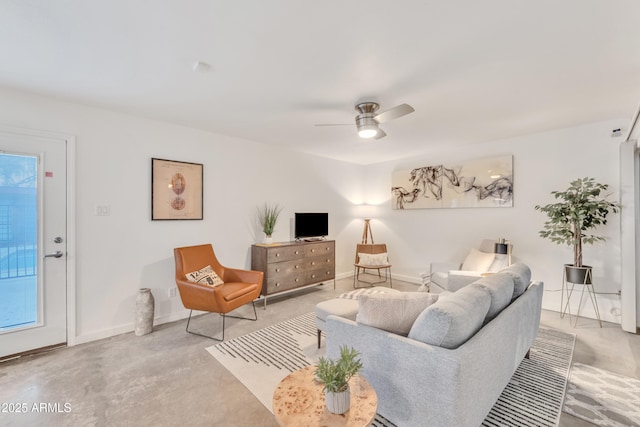 living area with baseboards, a ceiling fan, and concrete flooring