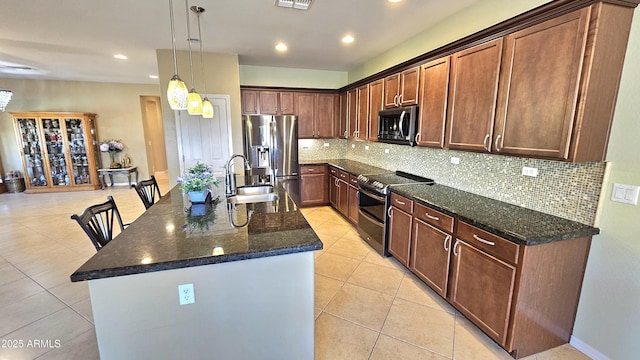 kitchen with appliances with stainless steel finishes, dark stone counters, a kitchen island with sink, sink, and light tile patterned floors