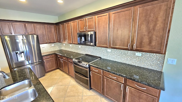 kitchen featuring decorative backsplash, appliances with stainless steel finishes, sink, light tile patterned floors, and dark stone countertops