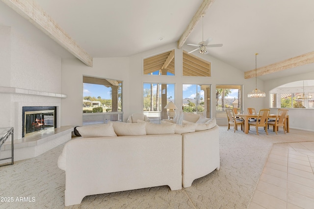 tiled living room featuring a tiled fireplace, a healthy amount of sunlight, ceiling fan with notable chandelier, and beam ceiling