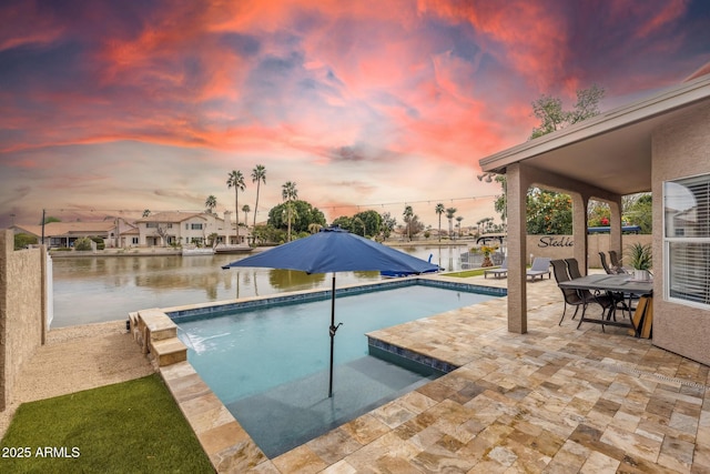 pool at dusk with a water view, a patio, and pool water feature