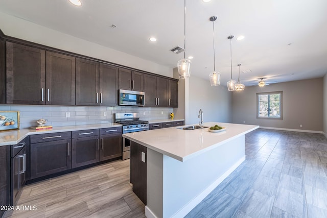 kitchen featuring appliances with stainless steel finishes, ceiling fan, a kitchen island with sink, sink, and hanging light fixtures