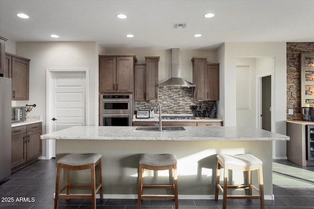 kitchen featuring wall chimney exhaust hood, a kitchen breakfast bar, and a kitchen island with sink