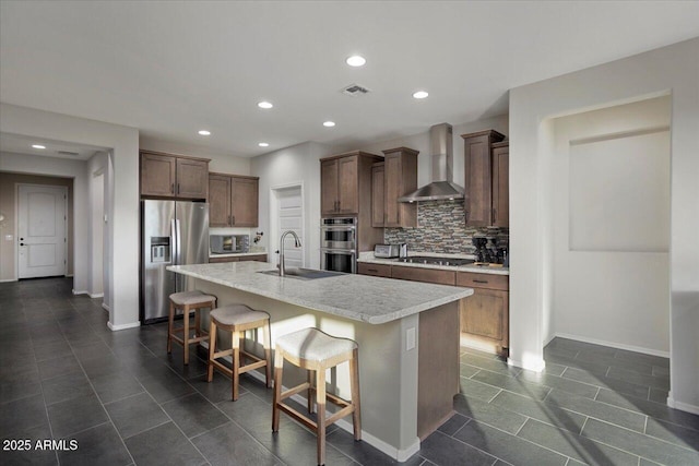 kitchen with sink, wall chimney range hood, a kitchen breakfast bar, an island with sink, and appliances with stainless steel finishes