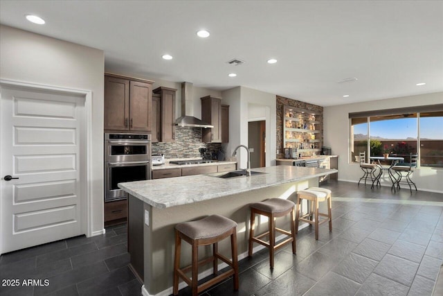 kitchen with sink, wall chimney range hood, a kitchen breakfast bar, a kitchen island with sink, and appliances with stainless steel finishes