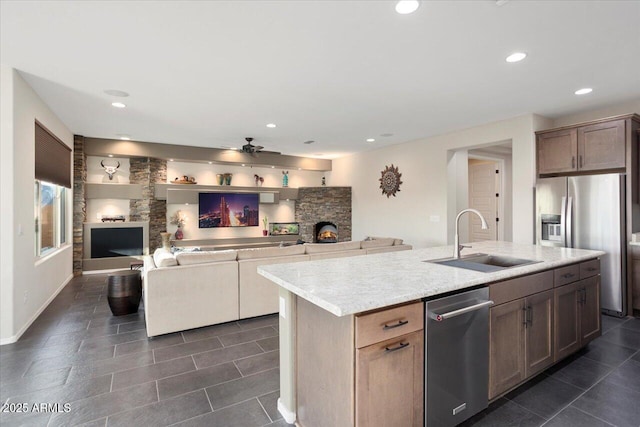 kitchen with a kitchen island with sink, sink, ceiling fan, light stone countertops, and stainless steel appliances