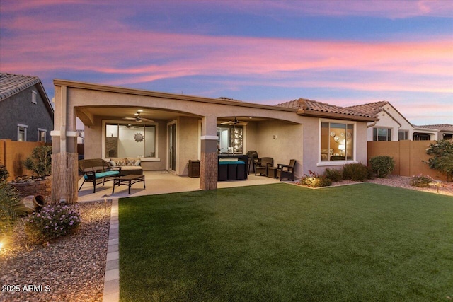 back house at dusk with a lawn, ceiling fan, a jacuzzi, an outdoor hangout area, and a patio area