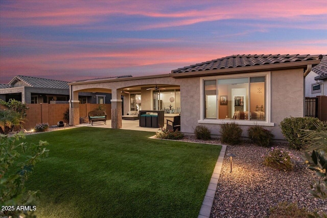 back house at dusk featuring a patio area, ceiling fan, and a yard