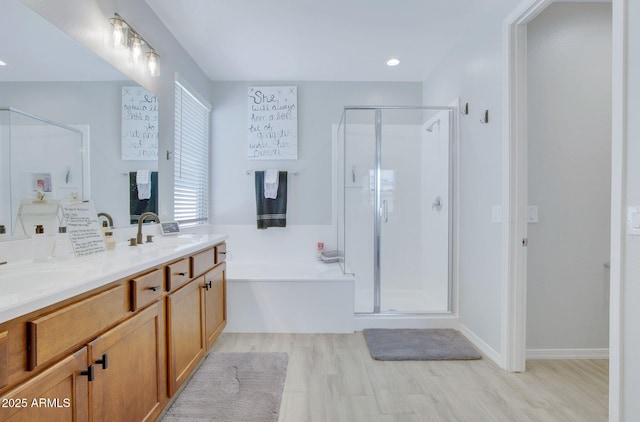 full bath with a sink, a shower stall, double vanity, a garden tub, and wood finished floors