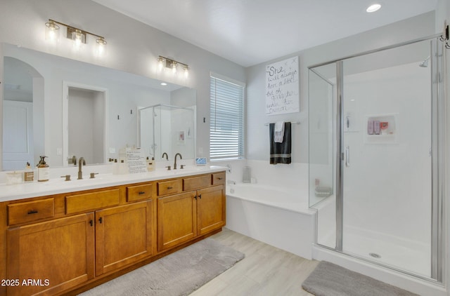 full bathroom featuring a shower stall, a sink, double vanity, a bath, and wood finished floors
